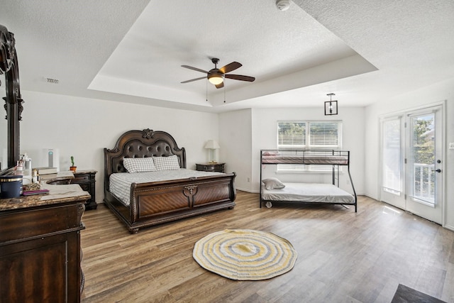 bedroom featuring a textured ceiling, access to outside, a tray ceiling, ceiling fan, and hardwood / wood-style floors