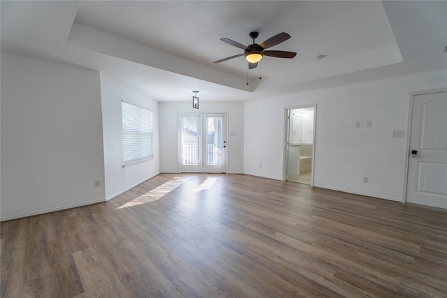 empty room featuring a tray ceiling, wood finished floors, a ceiling fan, and baseboards