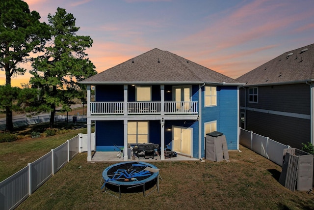 back house at dusk featuring a lawn, a patio area, and a balcony