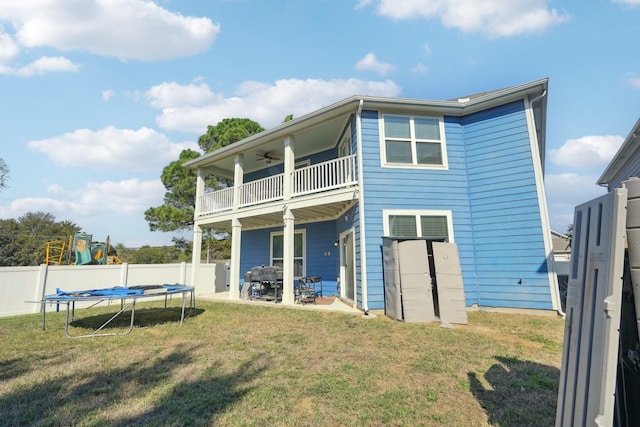 rear view of property with a lawn, a trampoline, ceiling fan, a balcony, and a patio