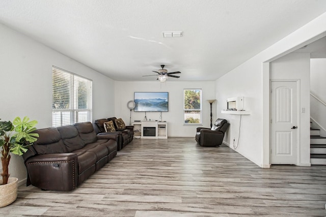 living room with ceiling fan, light wood-type flooring, and a textured ceiling