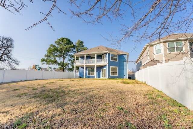 rear view of house featuring a lawn, a fenced backyard, and a balcony