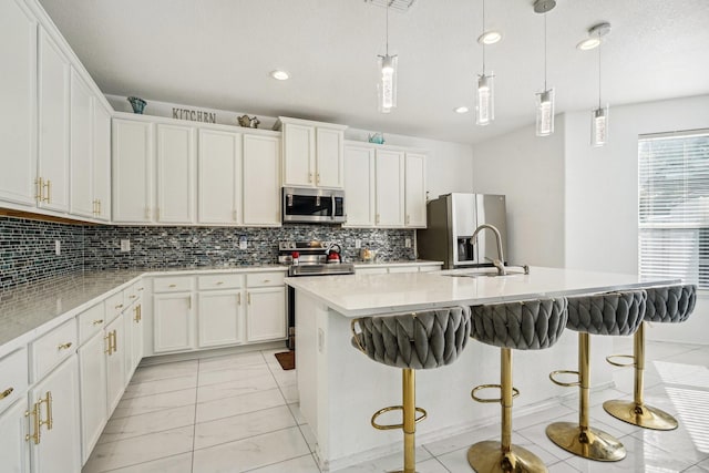 kitchen with a breakfast bar, pendant lighting, stainless steel appliances, and an island with sink