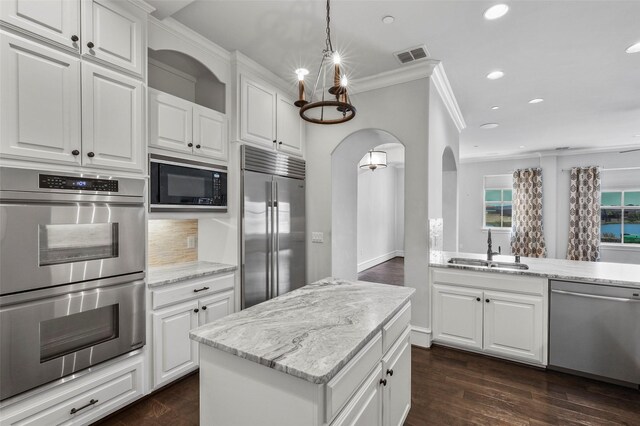 kitchen with white cabinetry, sink, built in appliances, pendant lighting, and a kitchen island