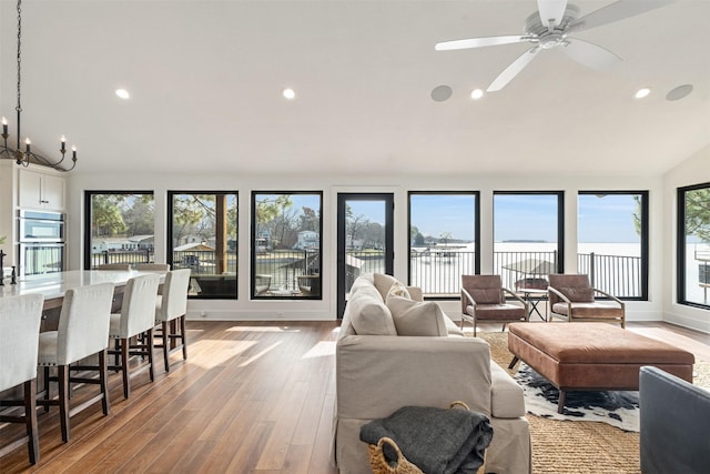 living room with hardwood / wood-style floors, ceiling fan with notable chandelier, a water view, and vaulted ceiling