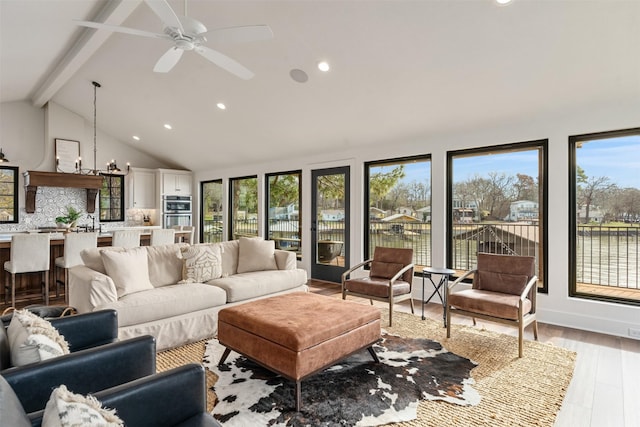 living room with ceiling fan with notable chandelier, lofted ceiling with beams, and light wood-type flooring