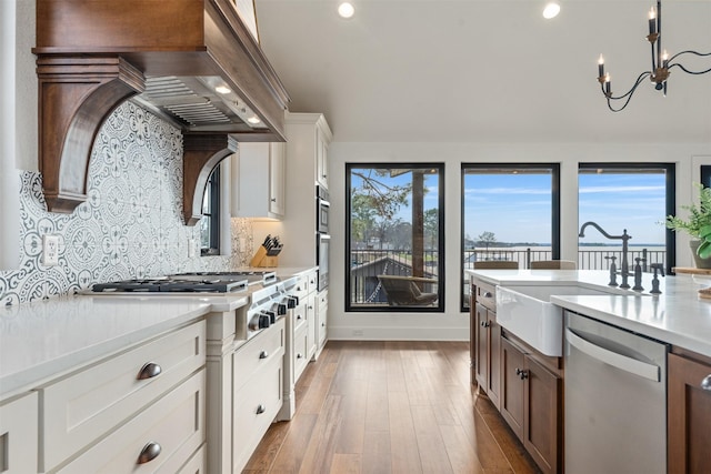 kitchen with white cabinetry, wall chimney range hood, backsplash, appliances with stainless steel finishes, and hardwood / wood-style flooring