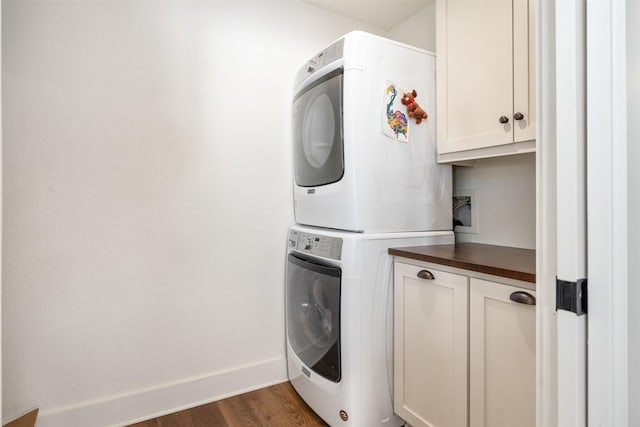 laundry room featuring cabinets, stacked washer / dryer, and dark wood-type flooring