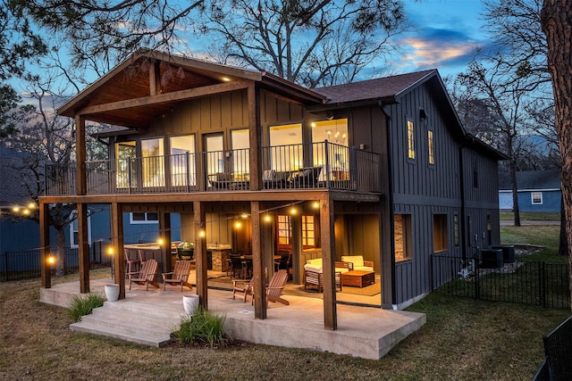 back house at dusk with a yard, a patio, a balcony, and an outdoor hangout area