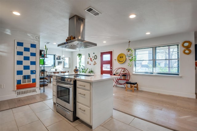 kitchen with island exhaust hood, stainless steel electric range oven, a kitchen island, white cabinetry, and light tile patterned flooring