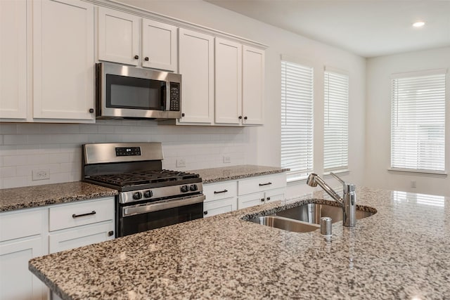 kitchen with light stone countertops, white cabinetry, sink, and appliances with stainless steel finishes