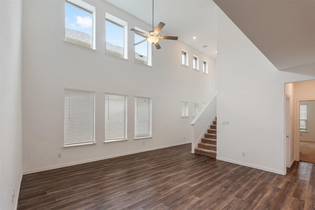 unfurnished living room with ceiling fan, dark wood-type flooring, and a high ceiling