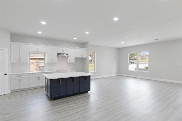 kitchen with a kitchen island, sink, white cabinets, backsplash, and light hardwood / wood-style flooring