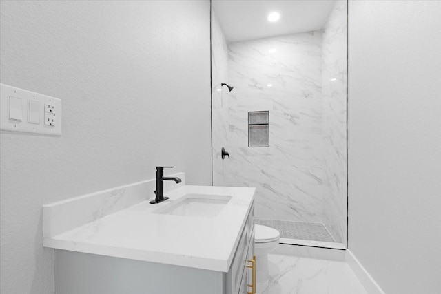 bathroom featuring a tile shower, vanity, and toilet