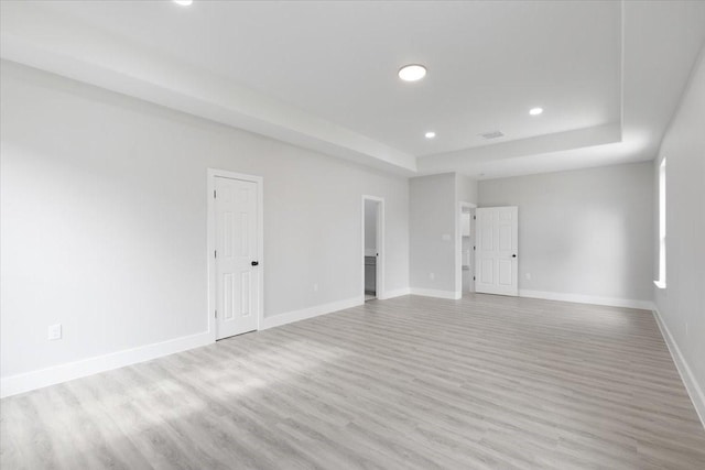 spare room with light hardwood / wood-style floors and a raised ceiling