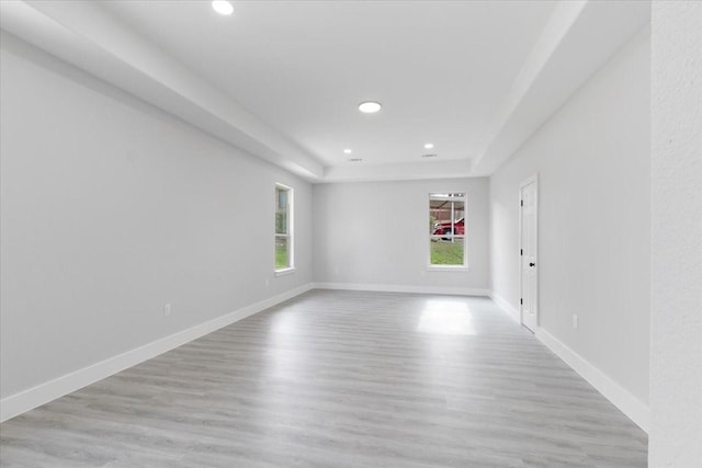 empty room featuring light wood-type flooring and a tray ceiling