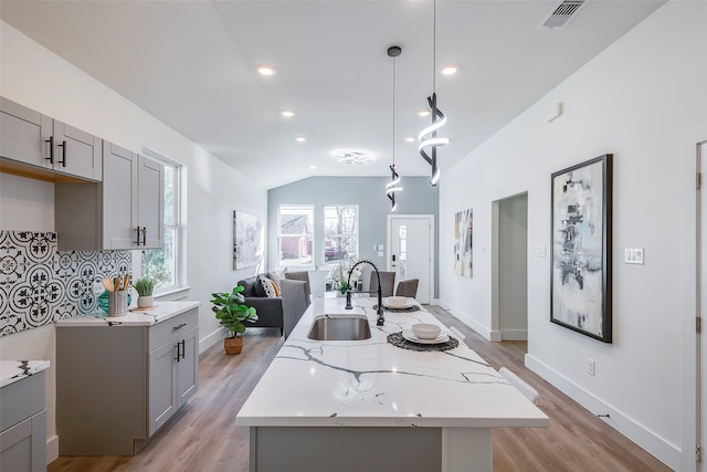 kitchen featuring a kitchen island with sink, sink, vaulted ceiling, gray cabinets, and decorative light fixtures