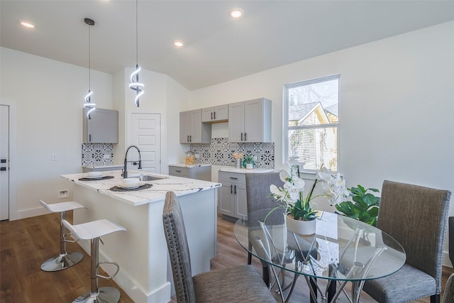 kitchen featuring gray cabinetry, a kitchen island with sink, hanging light fixtures, light stone countertops, and dark hardwood / wood-style flooring