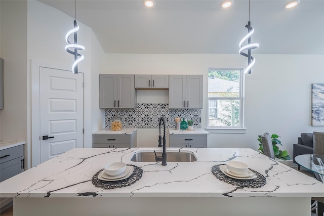 kitchen with gray cabinetry, sink, hanging light fixtures, backsplash, and a kitchen island with sink