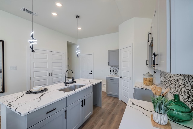 kitchen featuring decorative backsplash, dark wood-type flooring, sink, decorative light fixtures, and an island with sink