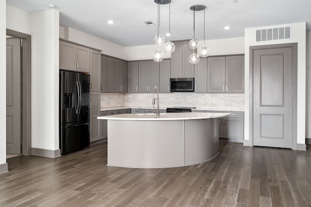 kitchen with dark hardwood / wood-style flooring, sink, black refrigerator with ice dispenser, and a center island with sink