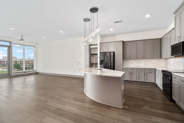 kitchen with gray cabinetry, a center island with sink, backsplash, and black appliances