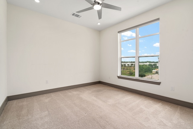 empty room with a wealth of natural light, light colored carpet, and ceiling fan