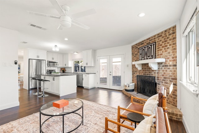 living room featuring a fireplace, ceiling fan, french doors, and dark wood-type flooring