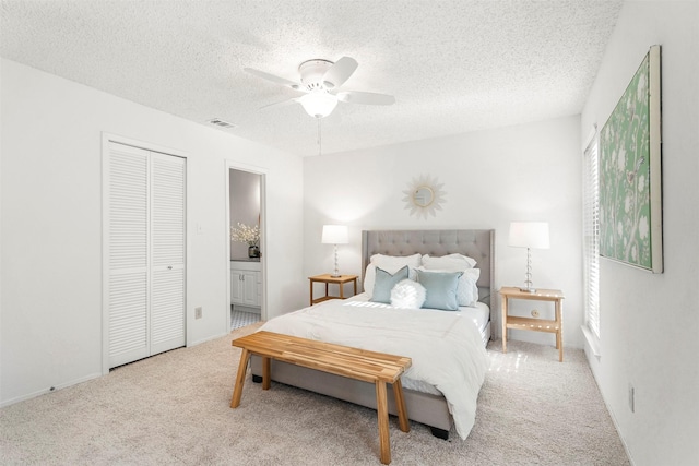 bedroom featuring ceiling fan, ensuite bathroom, a textured ceiling, light carpet, and a closet