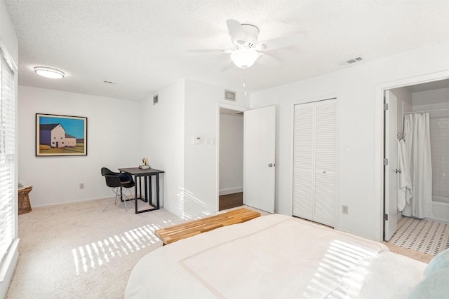 carpeted bedroom with a textured ceiling, a closet, ensuite bathroom, and ceiling fan