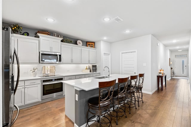 kitchen with appliances with stainless steel finishes, a kitchen breakfast bar, tasteful backsplash, sink, and a center island with sink