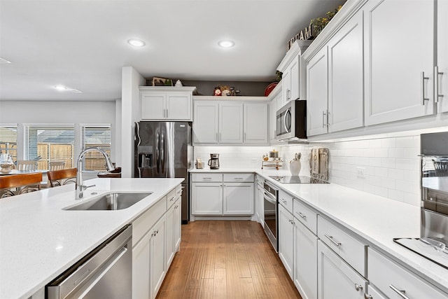 kitchen with sink, light hardwood / wood-style flooring, decorative backsplash, white cabinetry, and stainless steel appliances