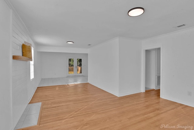 empty room featuring french doors, ornamental molding, and light hardwood / wood-style flooring