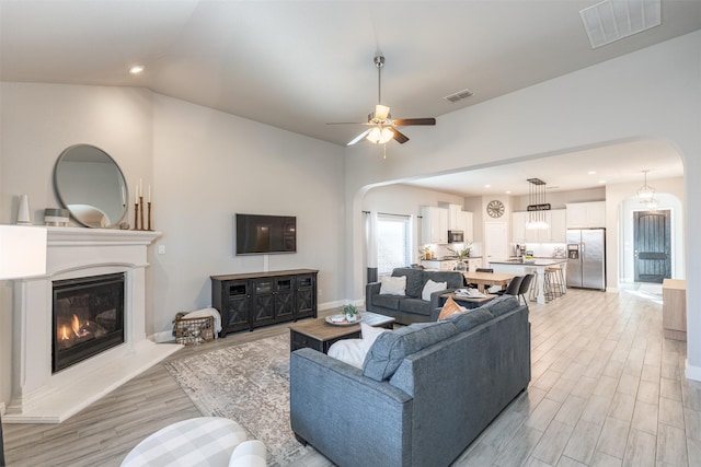 living room featuring light wood-style flooring, visible vents, and arched walkways