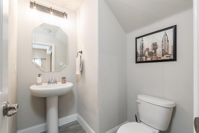 half bathroom featuring toilet, a sink, a textured ceiling, wood finished floors, and baseboards