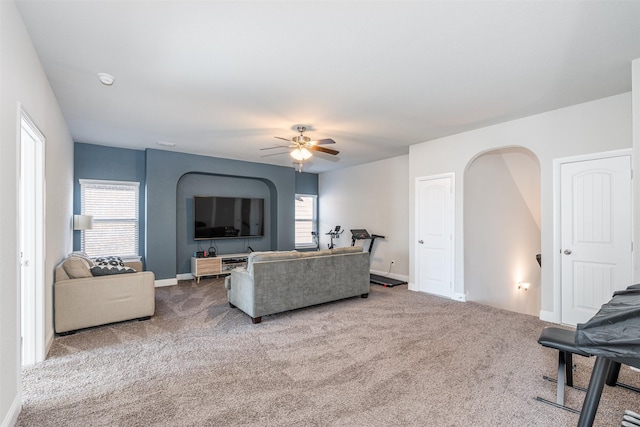 carpeted living area with a ceiling fan, arched walkways, a healthy amount of sunlight, and baseboards