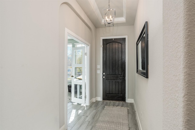 entryway with baseboards, a raised ceiling, wood finished floors, an inviting chandelier, and crown molding