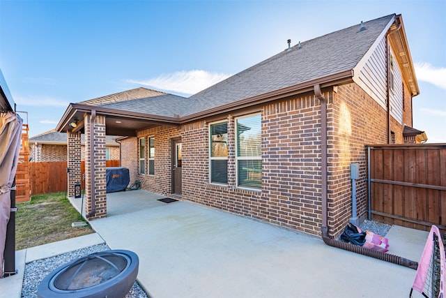 rear view of property featuring roof with shingles, fence, a patio, and brick siding