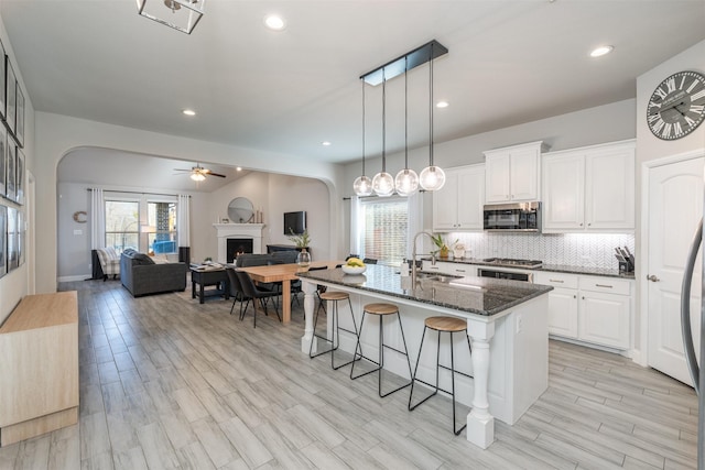 kitchen featuring a sink, a kitchen breakfast bar, a lit fireplace, appliances with stainless steel finishes, and decorative backsplash