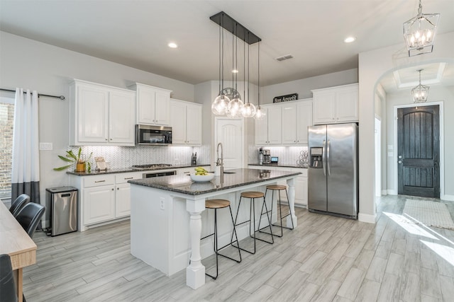 kitchen featuring stainless steel appliances, visible vents, white cabinetry, an island with sink, and a kitchen bar