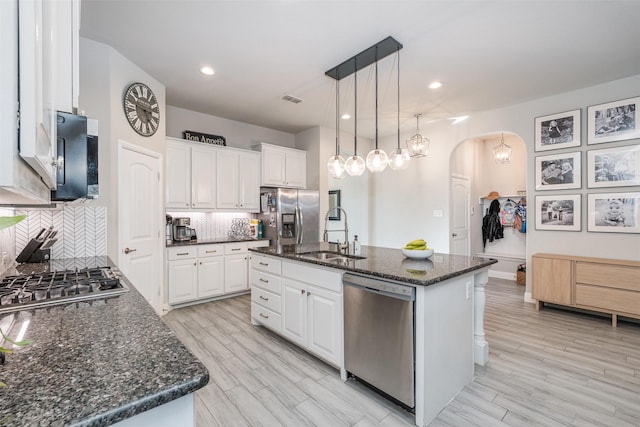 kitchen with arched walkways, stainless steel appliances, visible vents, white cabinetry, and a sink