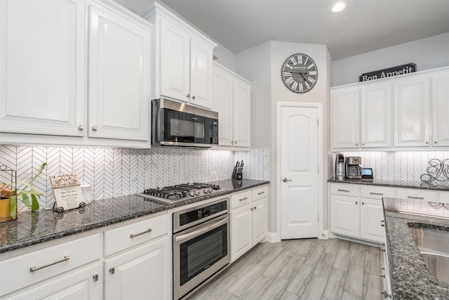 kitchen featuring white cabinets, appliances with stainless steel finishes, tasteful backsplash, and dark stone counters