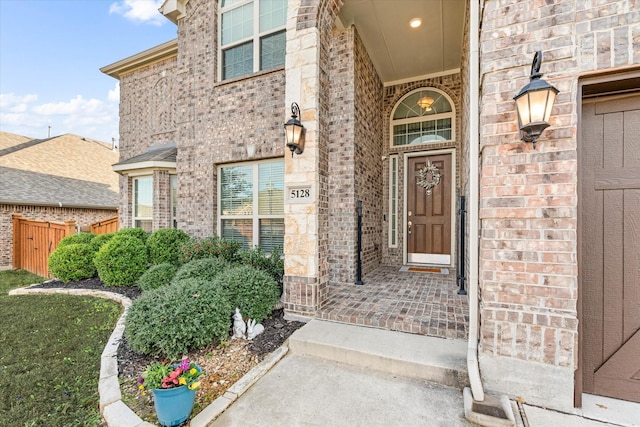 view of exterior entry featuring fence and brick siding