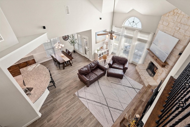 living room with ceiling fan, a stone fireplace, and a high ceiling