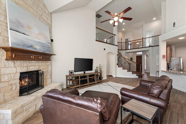 living room featuring hardwood / wood-style floors, a stone fireplace, high vaulted ceiling, and ceiling fan