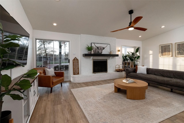 living room with ceiling fan, light hardwood / wood-style flooring, vaulted ceiling, and a brick fireplace