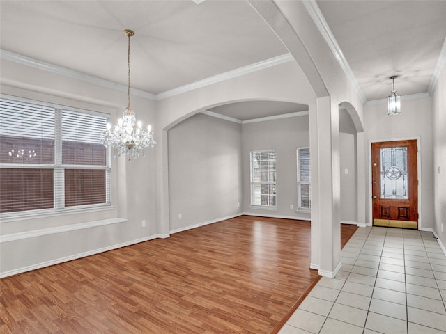 tiled foyer featuring crown molding, plenty of natural light, and an inviting chandelier