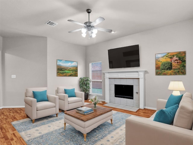 living room featuring hardwood / wood-style flooring, ceiling fan, and a tiled fireplace