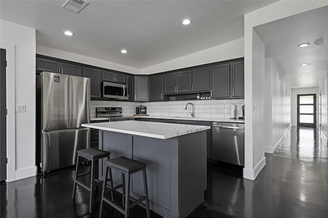 kitchen featuring sink, stainless steel appliances, tasteful backsplash, light stone counters, and a kitchen island