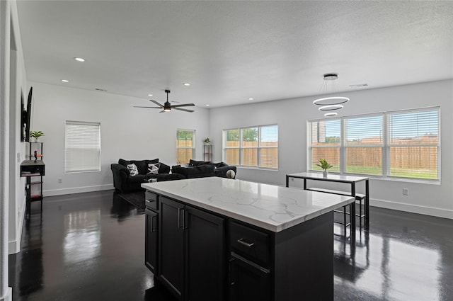 kitchen with ceiling fan, a center island, light stone counters, a textured ceiling, and decorative light fixtures